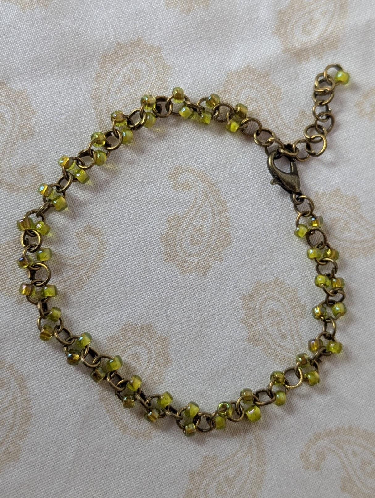 Bronze chain bracelet with paired green seed beads, featuring pink-lined green and silver-lined olive glass beads and a bronze lobster clasp.