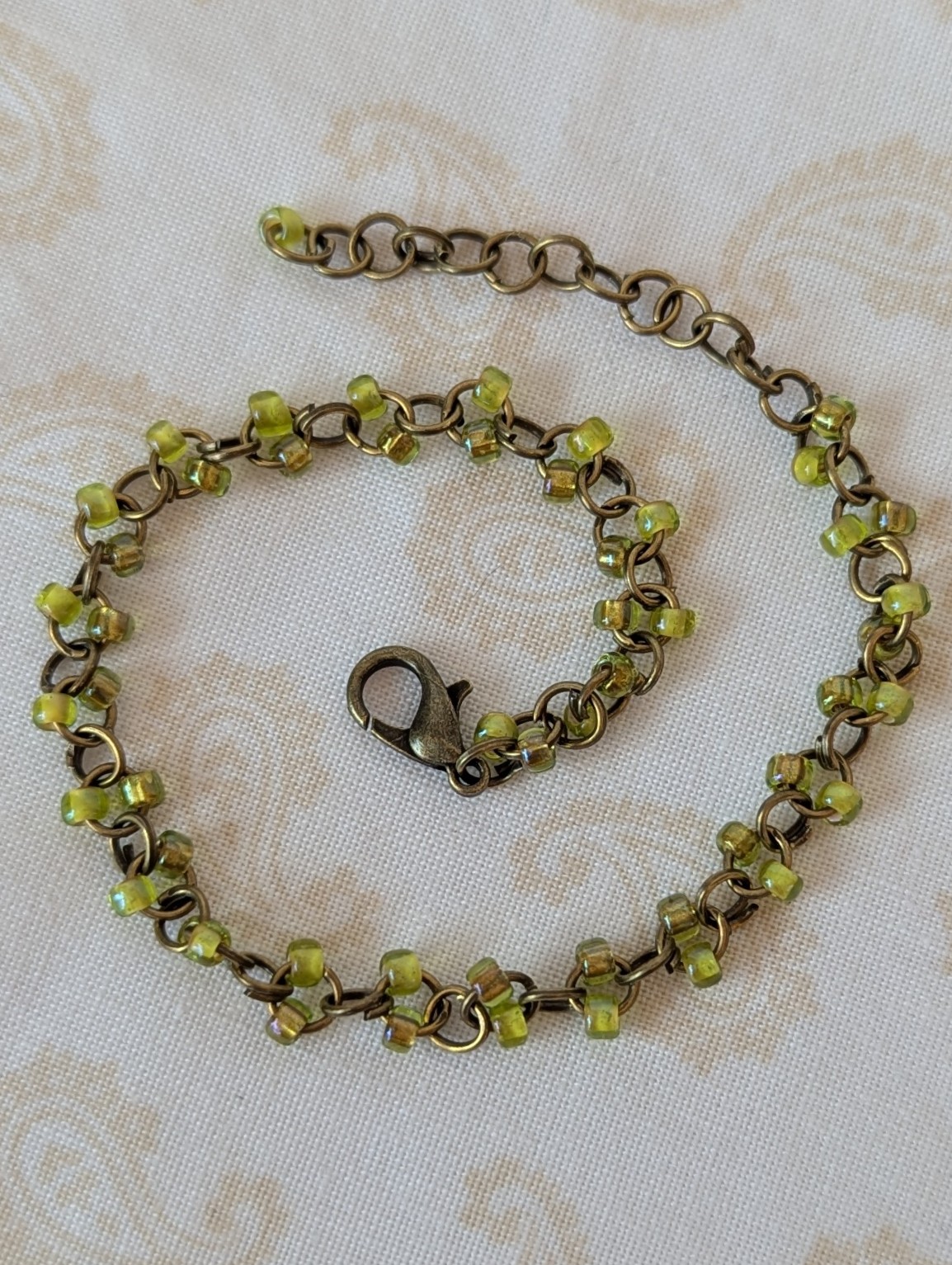 Bronze chain bracelet with paired green seed beads, featuring pink-lined green and silver-lined olive glass beads and a bronze lobster clasp.