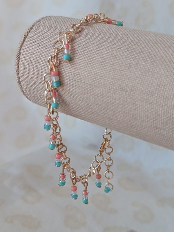 Rose-gold-colored chain bracelet with dangling seed bead trios the blush pink, pearl white, and soft sky blue of the trans flag, finished with a rose gold-colored lobster clasp.