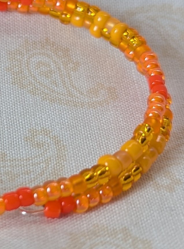 Orange memory wire bracelet with multiple shades and textures of orange glass beads, stretchy design with no clasp.
