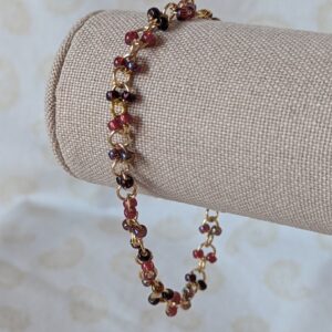 Gold chain bracelet with paired deep red seed beads in maroon, garnet, and iridescent wine tones, finished with a gold lobster clasp.