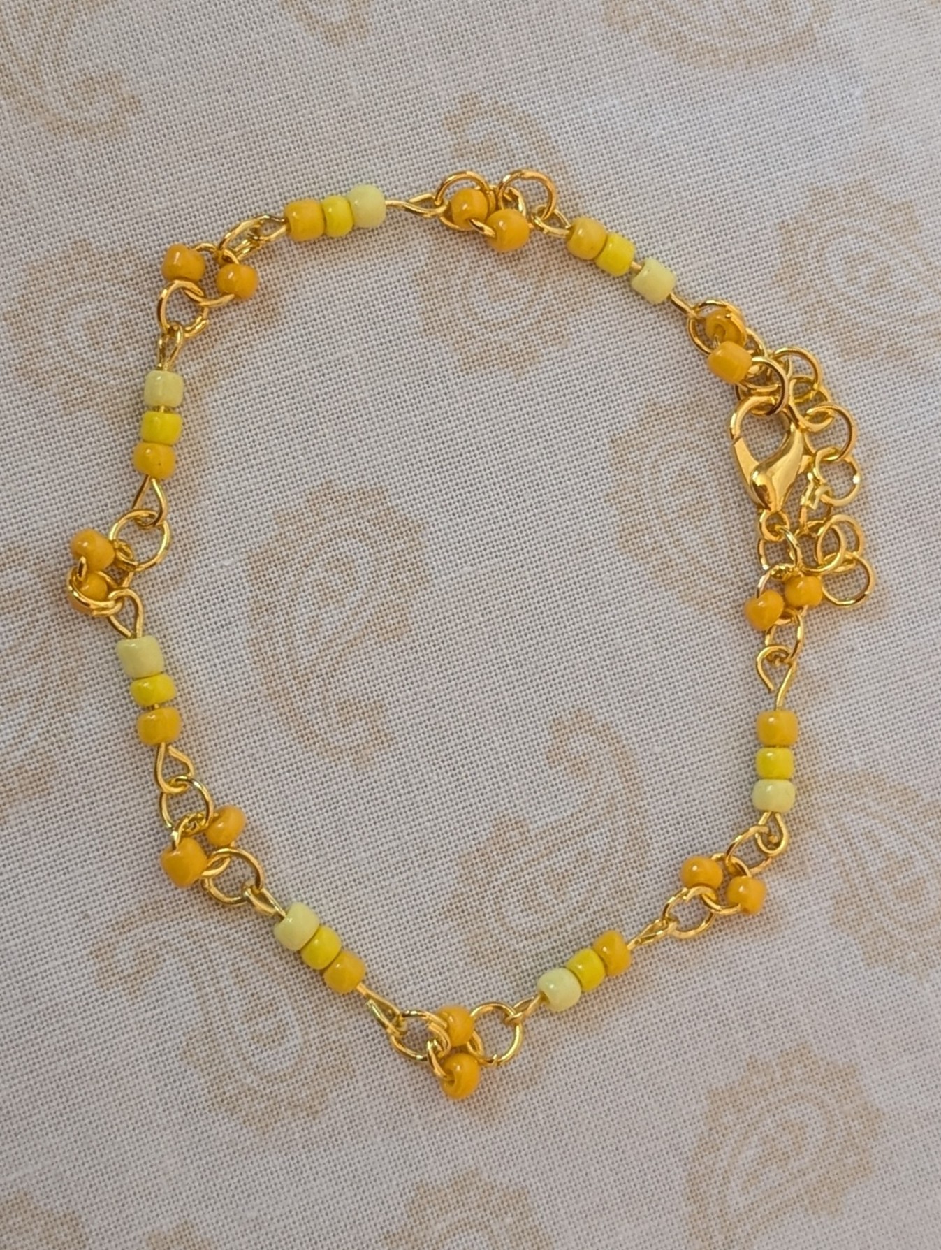 Handmade sunny yellow seed bead bracelet with gold chain links and lemon to marigold glass bead accents.
