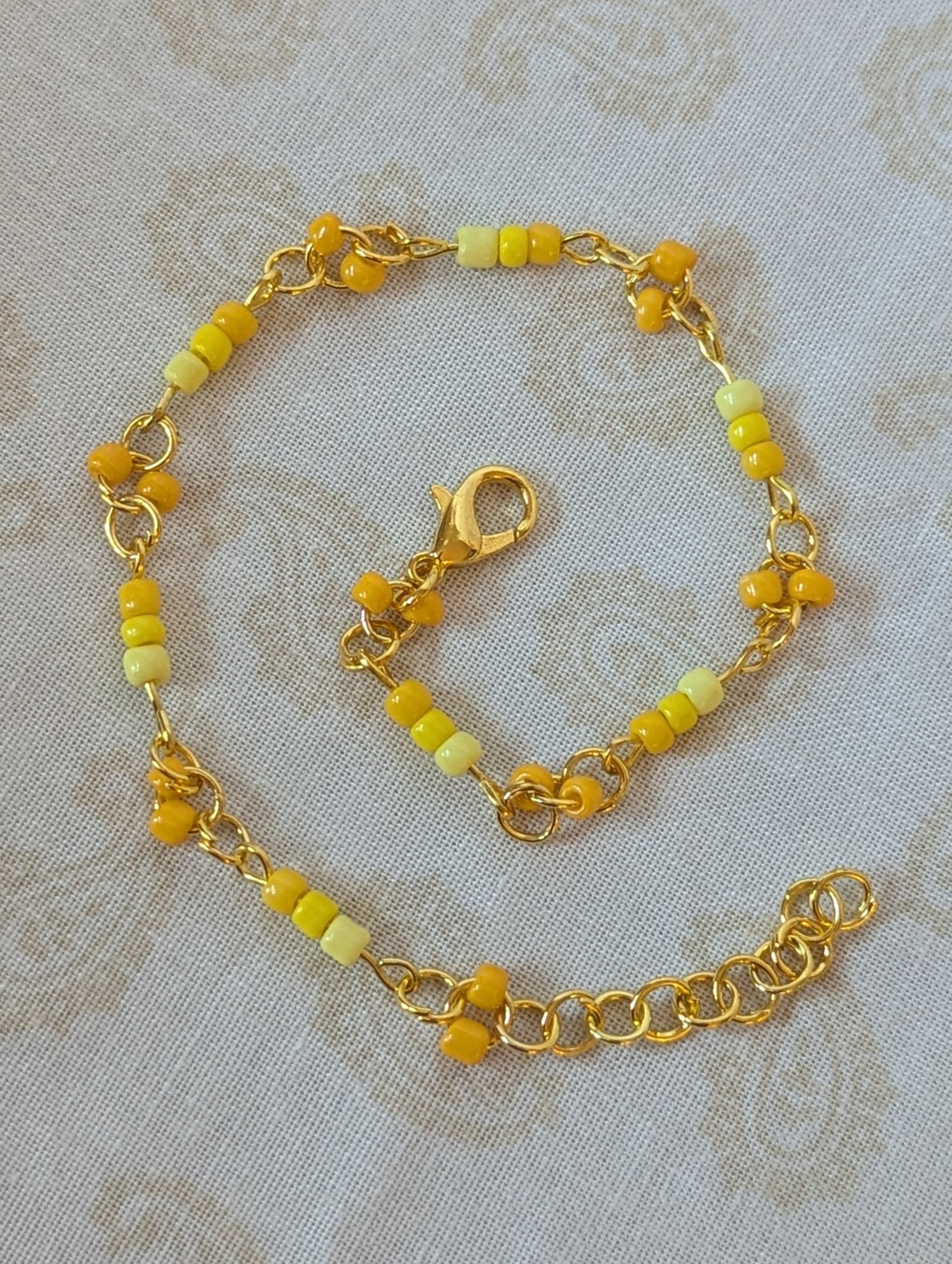 Handmade sunny yellow seed bead bracelet with gold chain links and lemon to marigold glass bead accents.