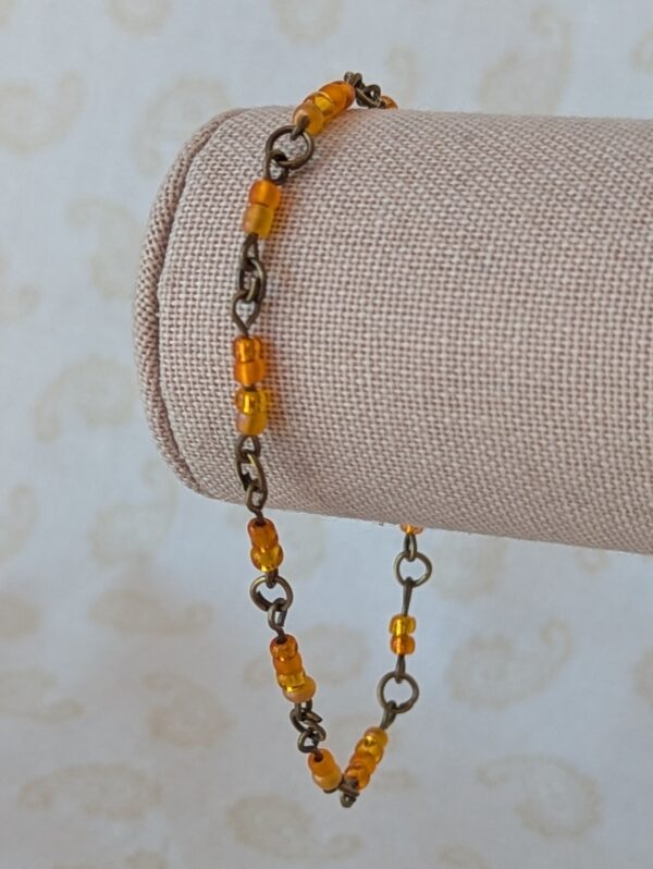 Handmade orange seed bead bracelet with bronze chain links and orange and yellow glass bead clusters.
