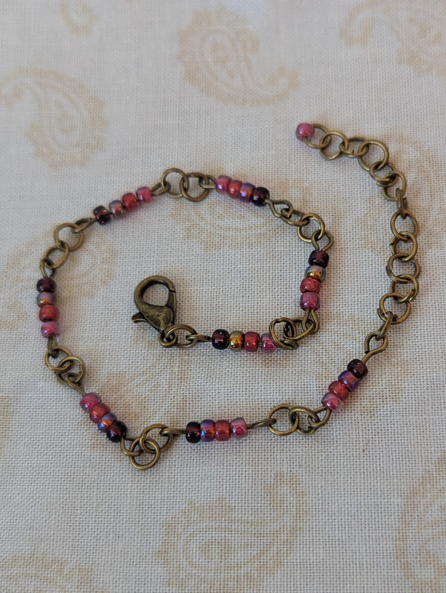 Handmade deep red gradient seed bead bracelet with bronze chain links and maroon and wine red glass bead clusters.