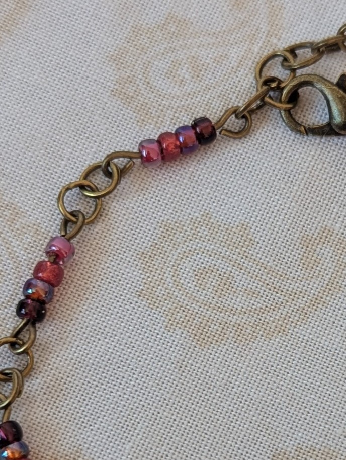 Handmade deep red gradient seed bead bracelet with bronze chain links and maroon and wine red glass bead clusters.