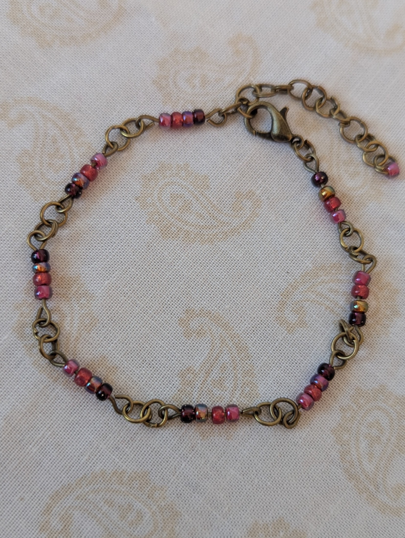 Handmade deep red gradient seed bead bracelet with bronze chain links and maroon and wine red glass bead clusters.