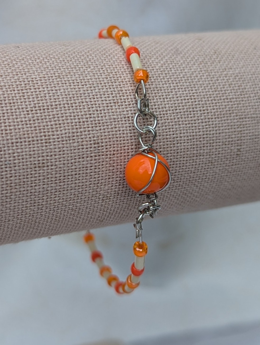 Handmade bracelet featuring cream bugle beads, vibrant orange seed beads, and a wire-wrapped Murano glass bead centerpiece on linked steel-colored memory wire with lobster clasp closure.