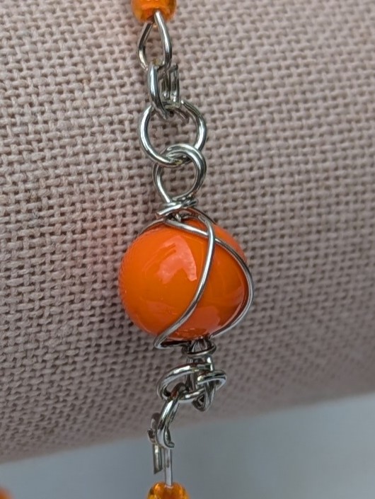 Handmade bracelet featuring cream bugle beads, vibrant orange seed beads, and a wire-wrapped Murano glass bead centerpiece on linked steel-colored memory wire with lobster clasp closure.