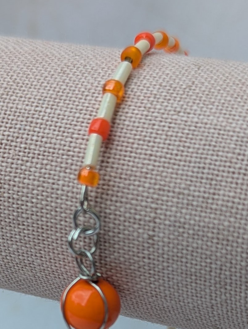 Handmade bracelet featuring cream bugle beads, vibrant orange seed beads, and a wire-wrapped Murano glass bead centerpiece on linked steel-colored memory wire with lobster clasp closure.