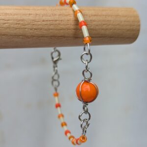 Handmade bracelet featuring cream bugle beads, vibrant orange seed beads, and a wire-wrapped Murano glass bead centerpiece on linked steel-colored memory wire with lobster clasp closure.