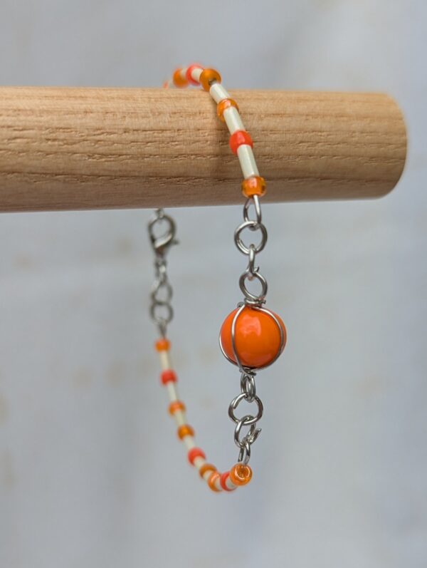 Handmade bracelet featuring cream bugle beads, vibrant orange seed beads, and a wire-wrapped Murano glass bead centerpiece on linked steel-colored memory wire with lobster clasp closure.