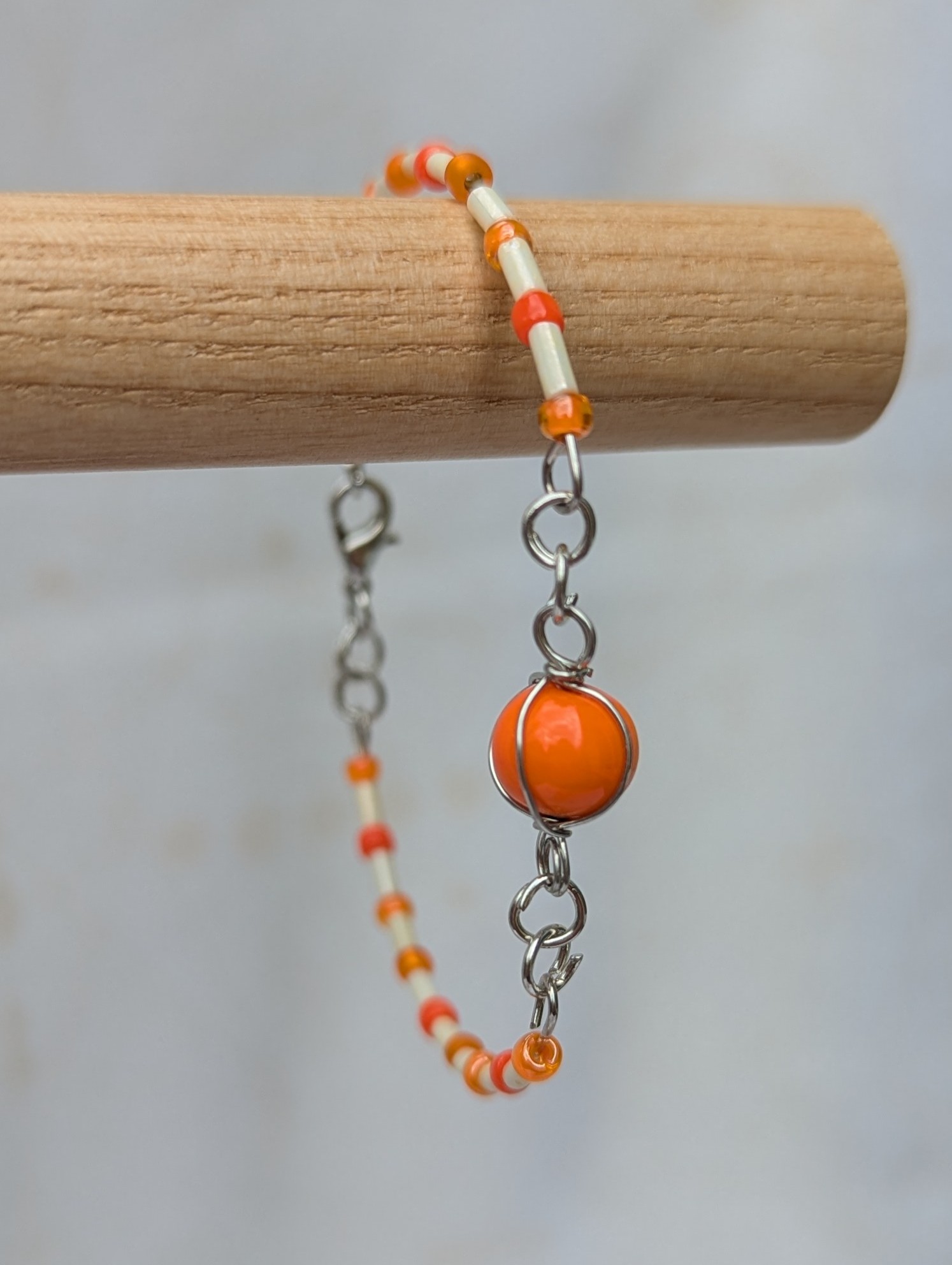 Handmade bracelet featuring cream bugle beads, vibrant orange seed beads, and a wire-wrapped Murano glass bead centerpiece on linked steel-colored memory wire with lobster clasp closure.