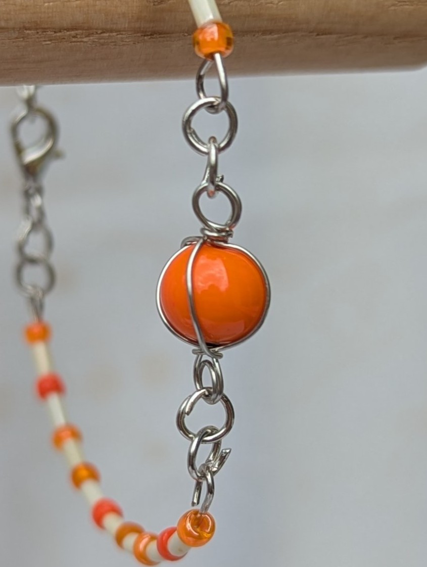 Handmade bracelet featuring cream bugle beads, vibrant orange seed beads, and a wire-wrapped Murano glass bead centerpiece on linked steel-colored memory wire with lobster clasp closure.