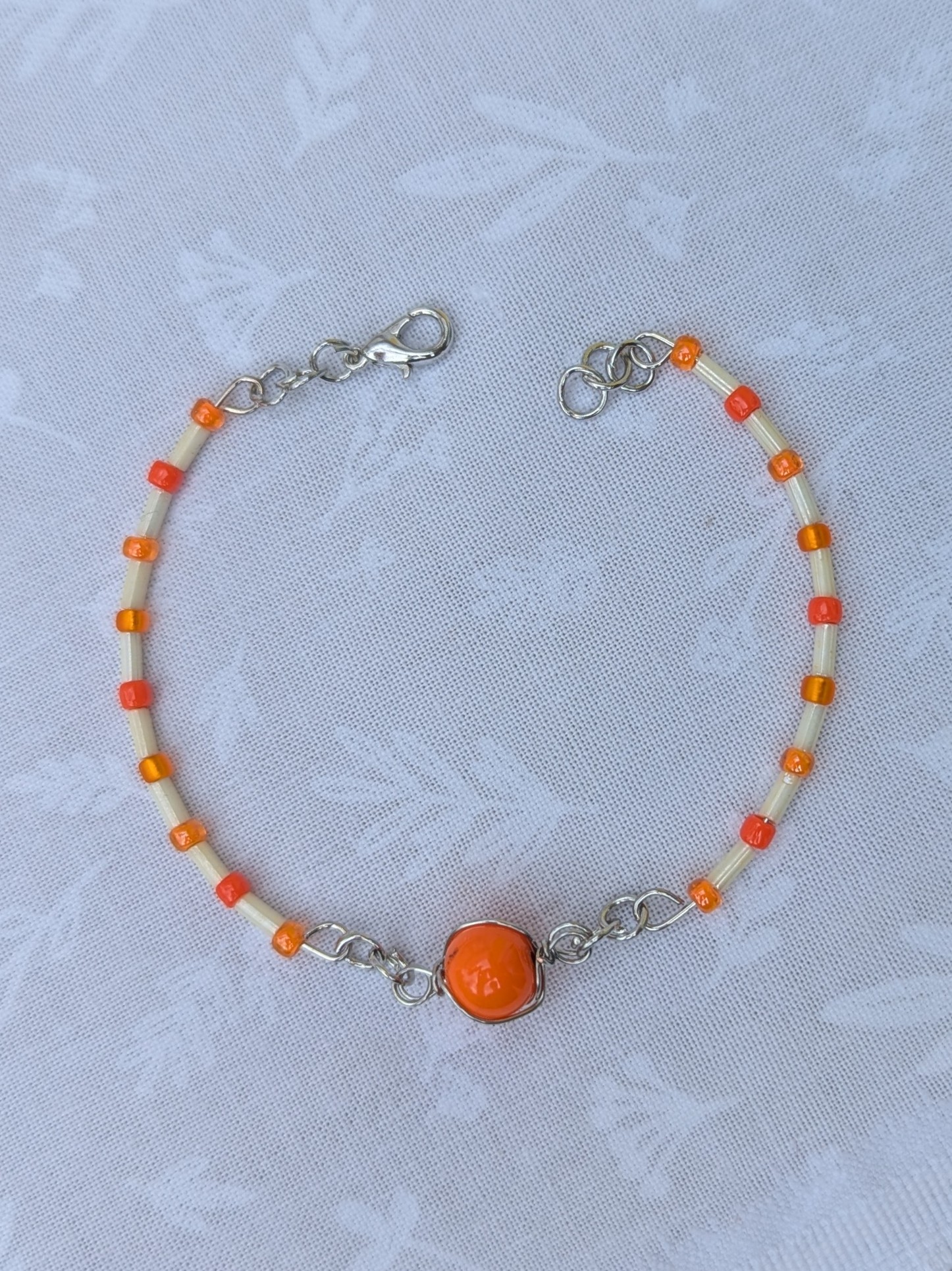 Handmade bracelet featuring cream bugle beads, vibrant orange seed beads, and a wire-wrapped Murano glass bead centerpiece on linked steel-colored memory wire with lobster clasp closure.