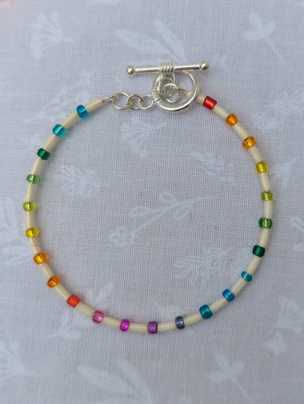 Handmade rainbow bracelet with cream bugle beads, multicolored glass seed beads, silver-colored memory wire, and toggle clasp closure.