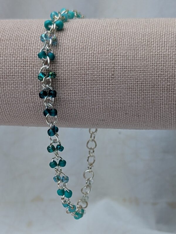 Handmade silver-colored chain bracelet with paired glass seed beads in a seafoam to deep teal gradient and toggle clasp closure.