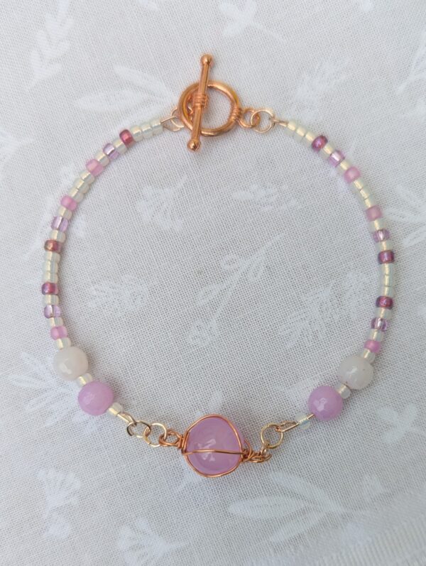 Handmade rose gold memory wire bracelet with lavender purple and ivory beads, copper wire-wrapped stone centerpiece, and copper toggle clasp.