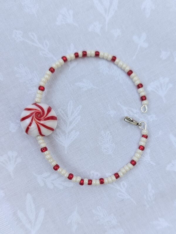 Handmade bracelet with red and pearl white seed beads and a glass peppermint swirl focal bead with silver clasp closure.