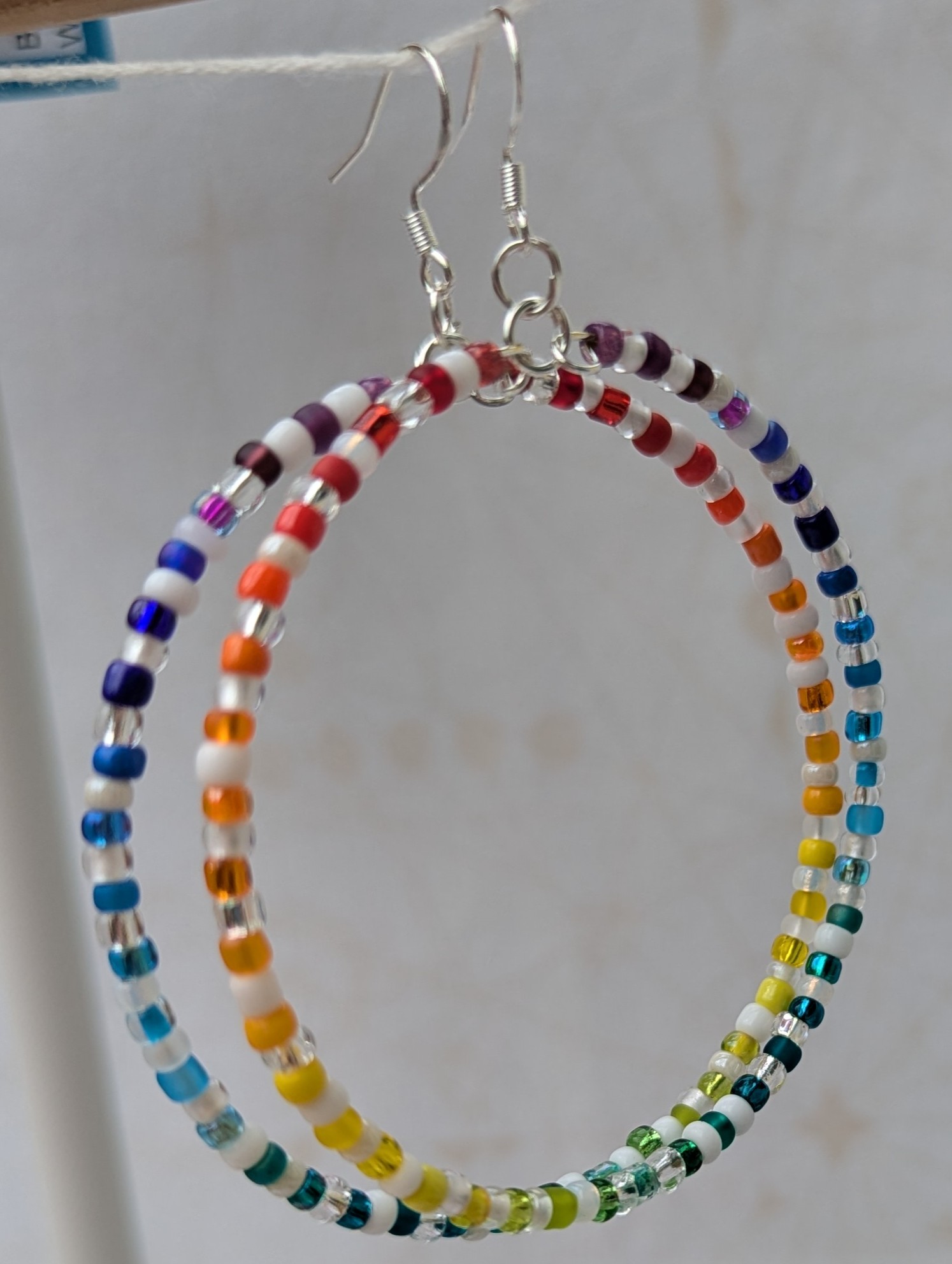 Handmade rainbow and white hoop earrings with silver-colored memory wire, multicolored glass seed beads, white and clear accent beads, and sterling silver French hooks.