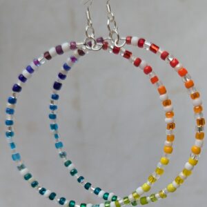 Handmade rainbow and white hoop earrings with silver-colored memory wire, multicolored glass seed beads, white and clear accent beads, and sterling silver French hooks.