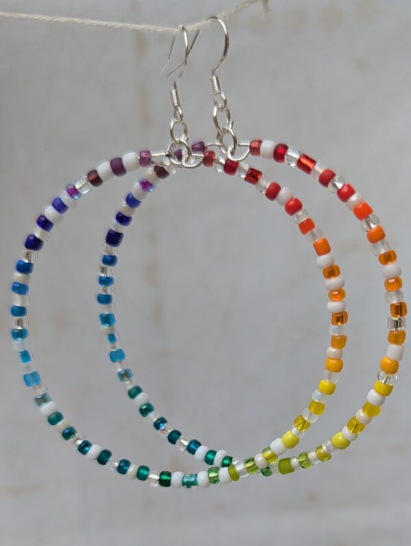 Handmade rainbow and white hoop earrings with silver-colored memory wire, multicolored glass seed beads, white and clear accent beads, and sterling silver French hooks.