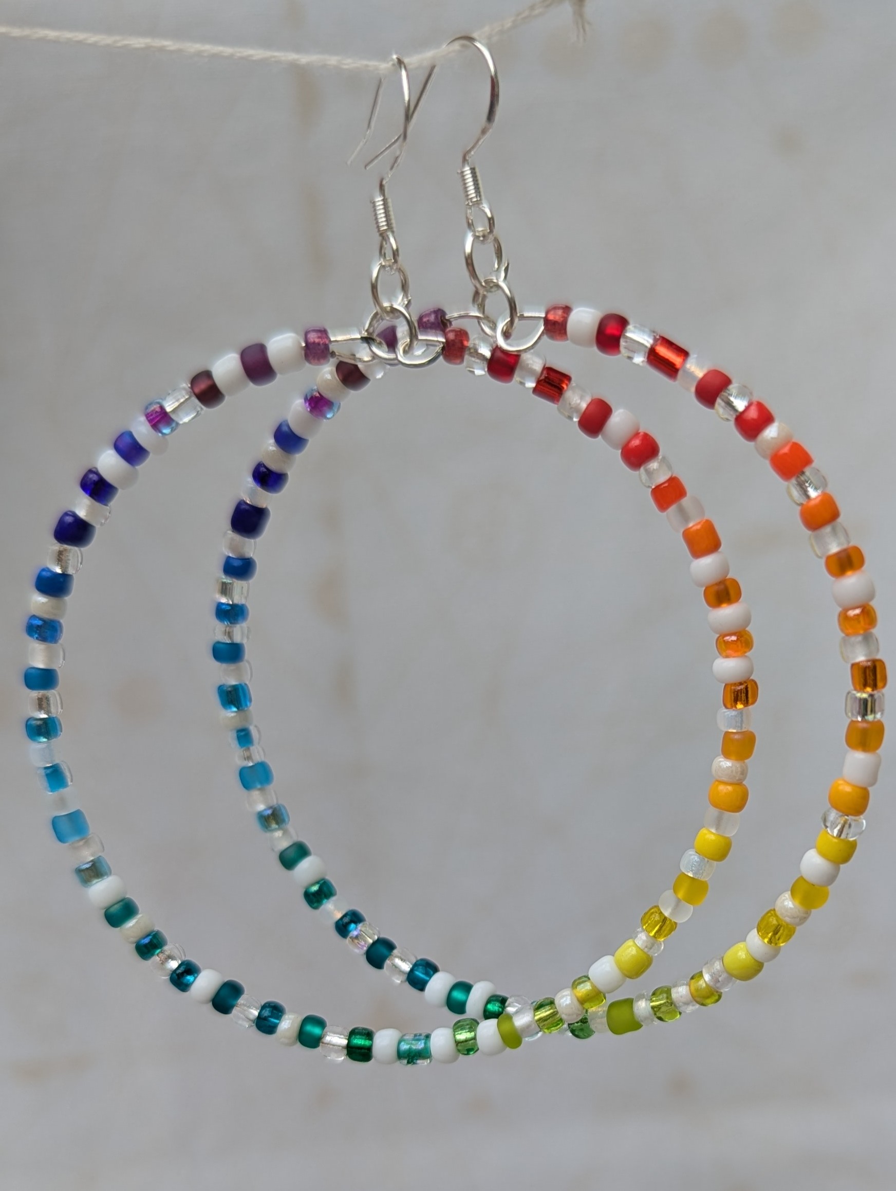 Handmade rainbow and white hoop earrings with silver-colored memory wire, multicolored glass seed beads, white and clear accent beads, and sterling silver French hooks.