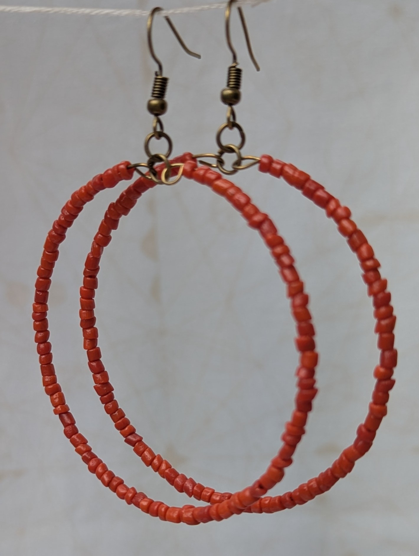 Handmade coral red beaded hoop earrings on bronze-colored memory wire with matching bronze French hooks.