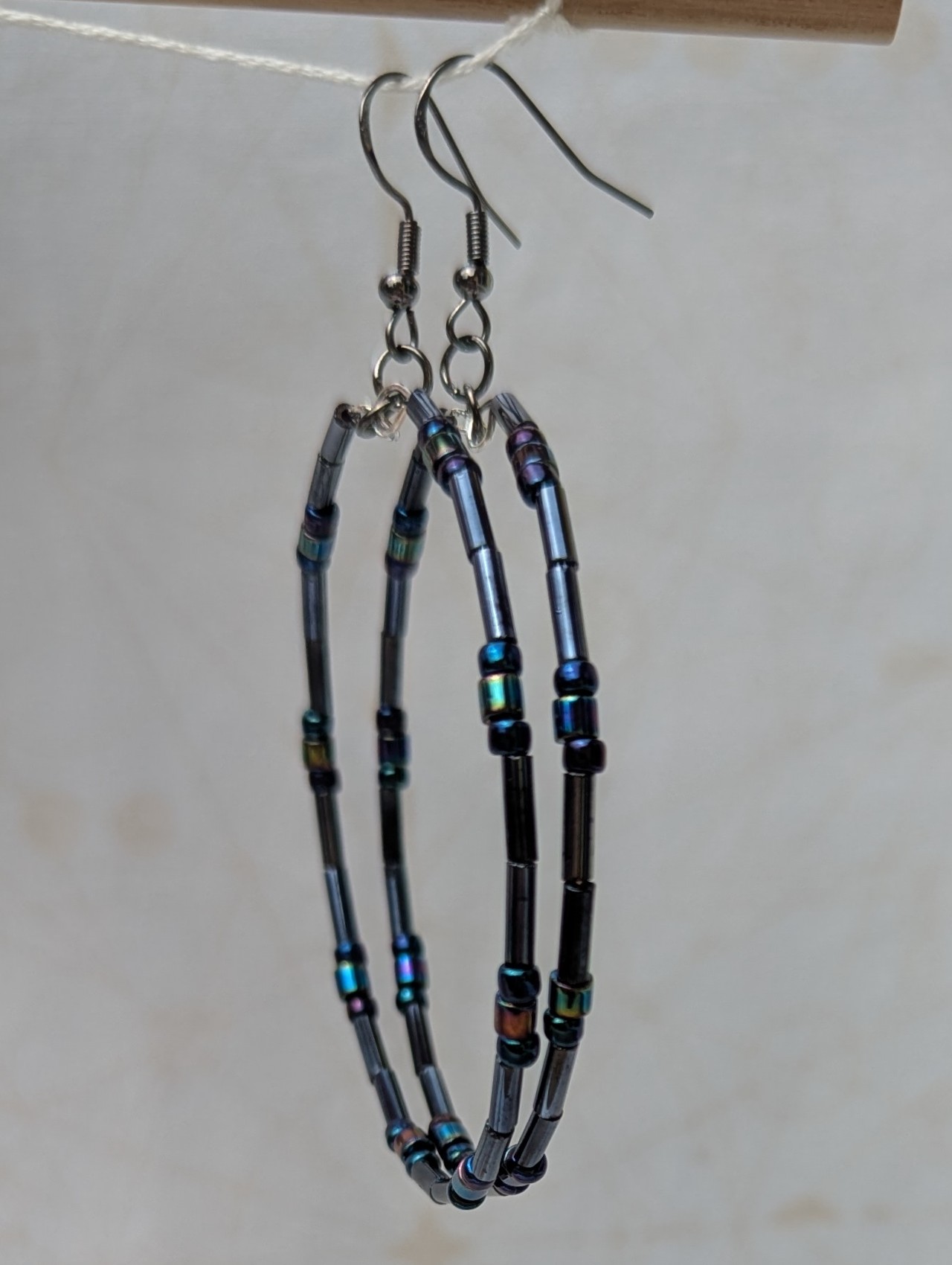 Handmade blue-black metallic hoop earrings with iridescent glass beads on steel-colored memory wire and tungsten-colored French hooks.