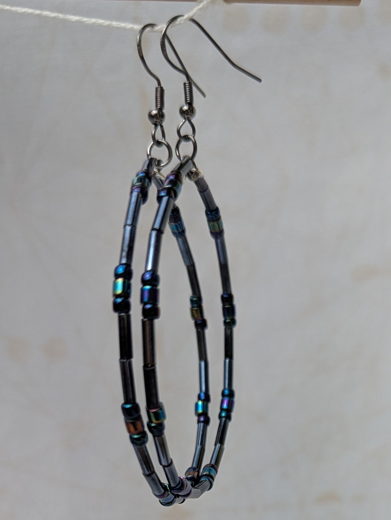 Handmade blue-black metallic hoop earrings with iridescent glass beads on steel-colored memory wire and tungsten-colored French hooks.