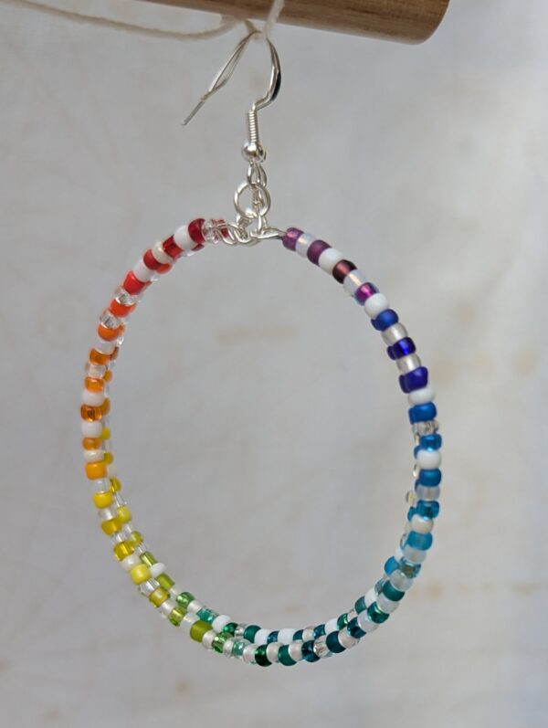 Handmade rainbow hoop earrings with silver-colored memory wire, multicolored glass seed beads, white and clear accent beads, and sterling silver French hooks.