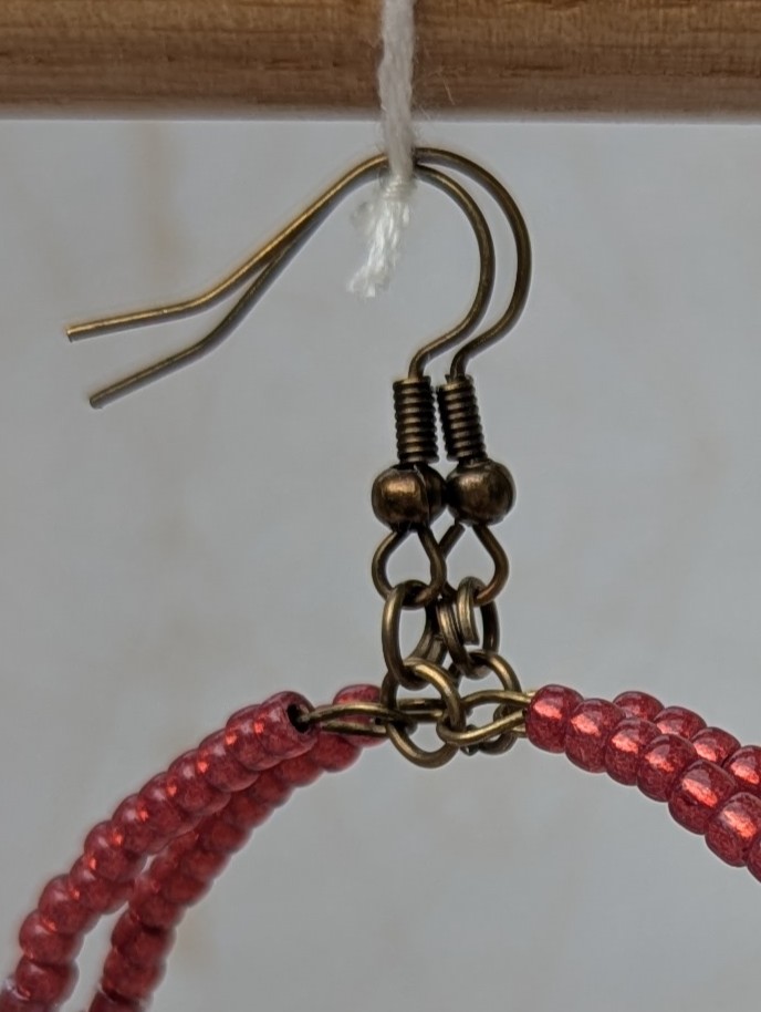 Handmade bronze hoop earrings with scarlet, garnet, raspberry, and wine-red glass beads in mixed shapes and textures on memory wire.