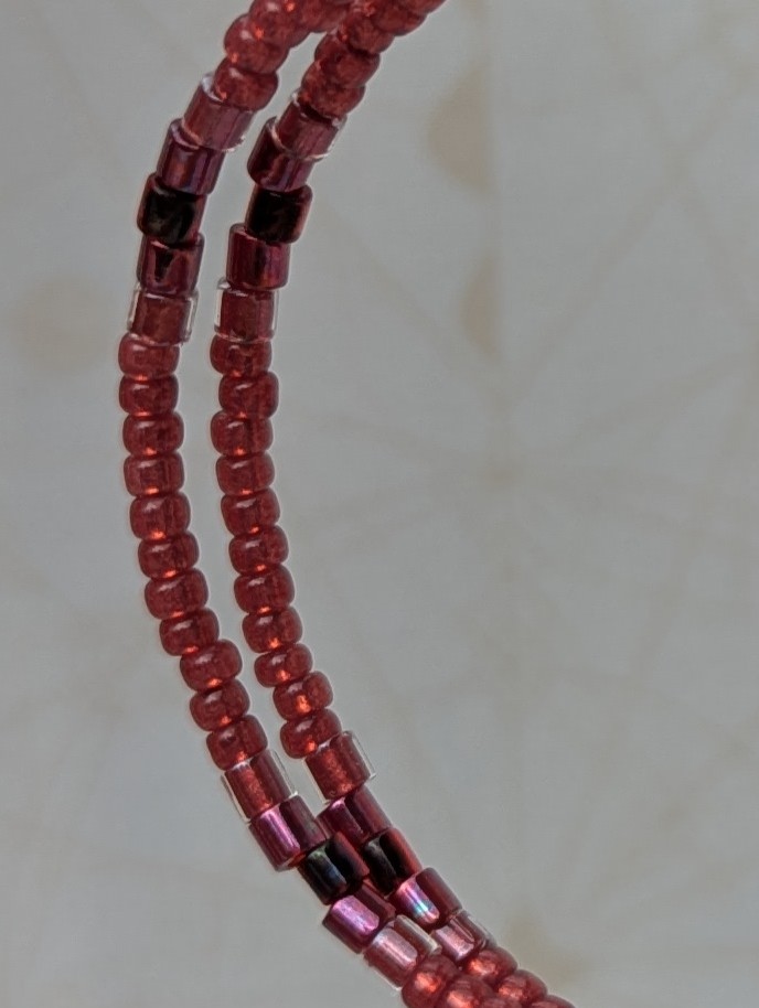 Handmade bronze hoop earrings with scarlet, garnet, raspberry, and wine-red glass beads in mixed shapes and textures on memory wire.