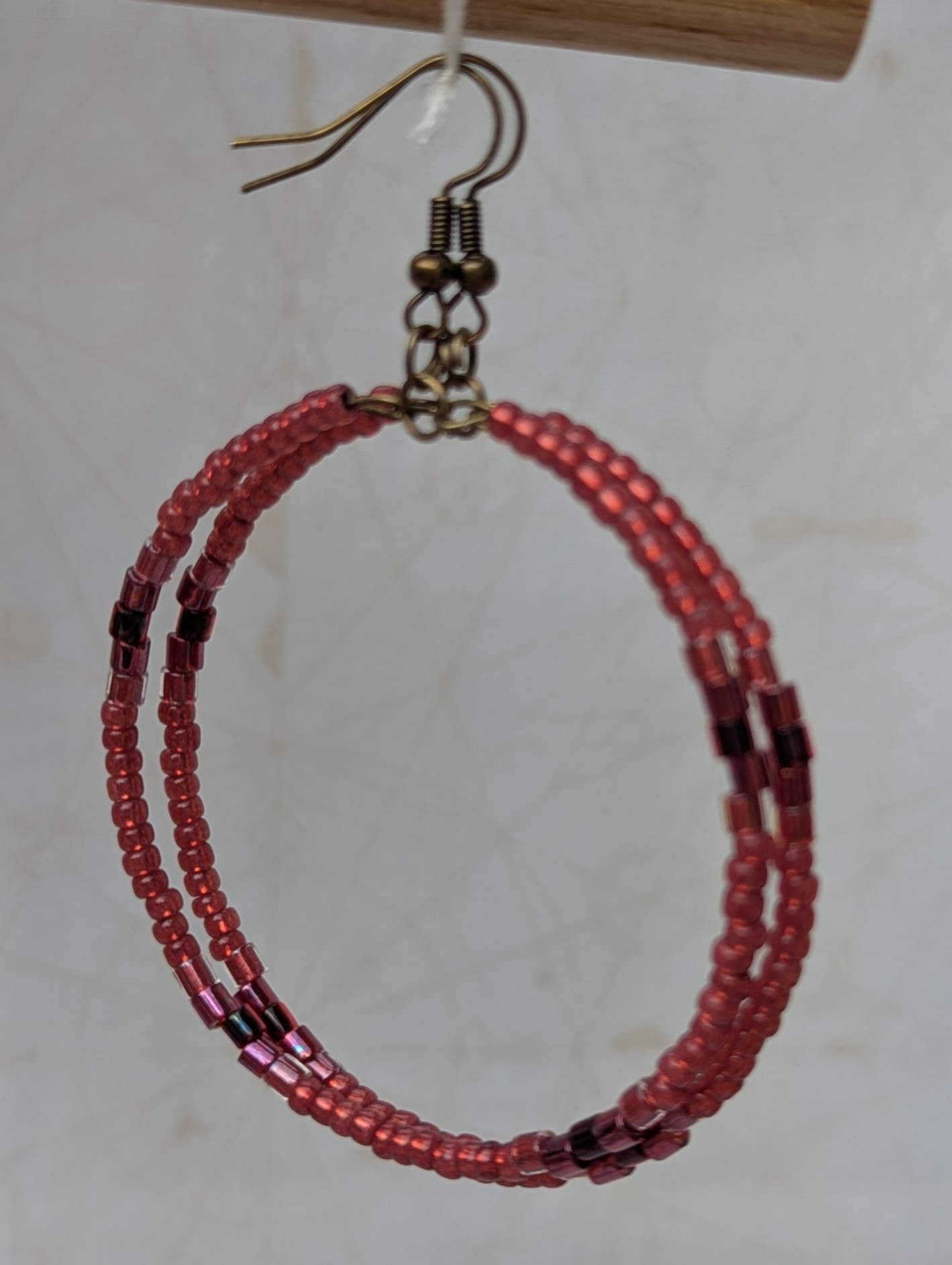 Handmade bronze hoop earrings with scarlet, garnet, raspberry, and wine-red glass beads in mixed shapes and textures on memory wire.