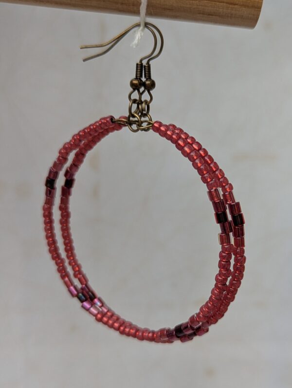Handmade bronze hoop earrings with scarlet, garnet, raspberry, and wine-red glass beads in mixed shapes and textures on memory wire.