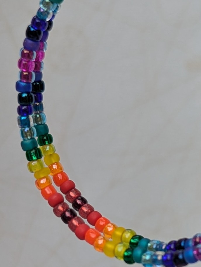 Handmade rainbow gradient hoop earrings with multicolored glass seed beads on silver memory wire and sterling silver French hooks.