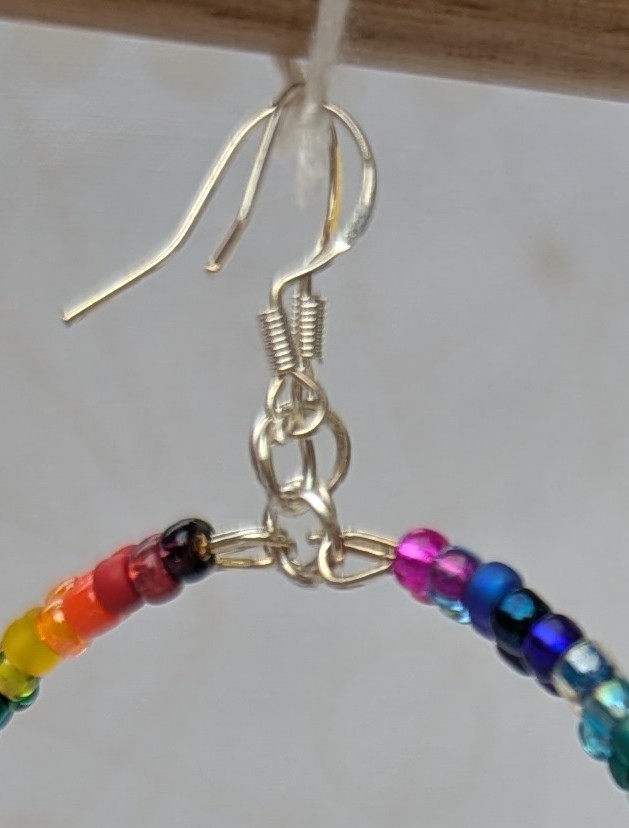 Handmade rainbow gradient hoop earrings with multicolored glass seed beads on silver memory wire and sterling silver French hooks.