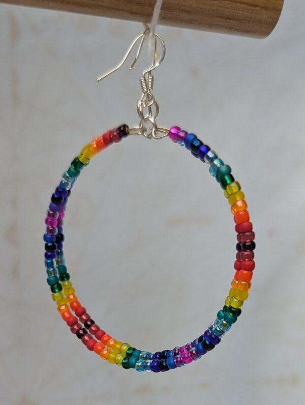 Handmade rainbow gradient hoop earrings with multicolored glass seed beads on silver memory wire and sterling silver French hooks.