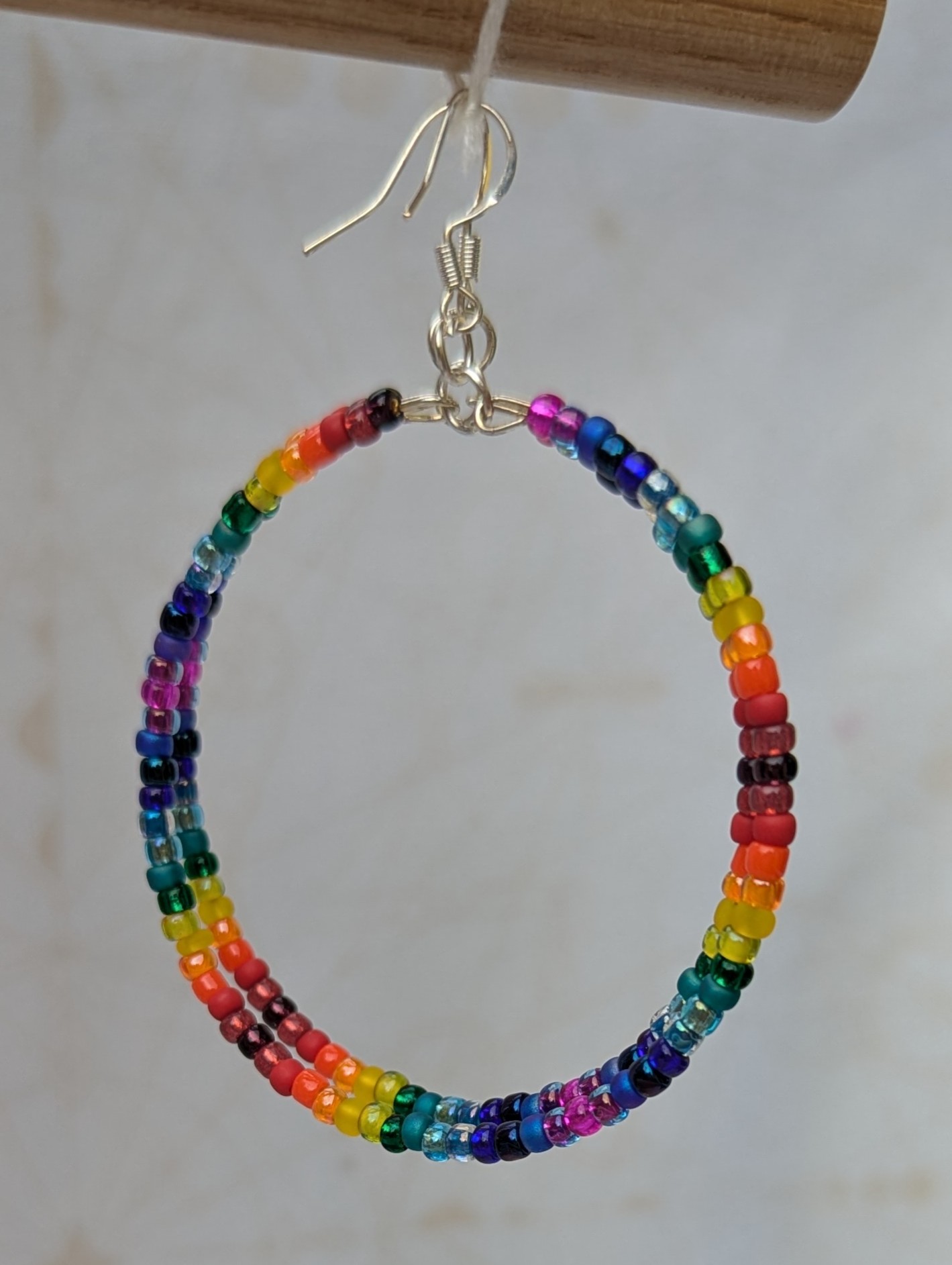 Handmade rainbow gradient hoop earrings with multicolored glass seed beads on silver memory wire and sterling silver French hooks.