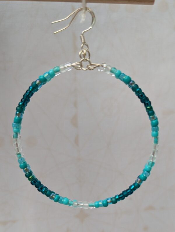 Handmade teal gradient hoop earrings with aqua, turquoise, and ocean-blue glass beads on silver memory wire and sterling silver French hooks.