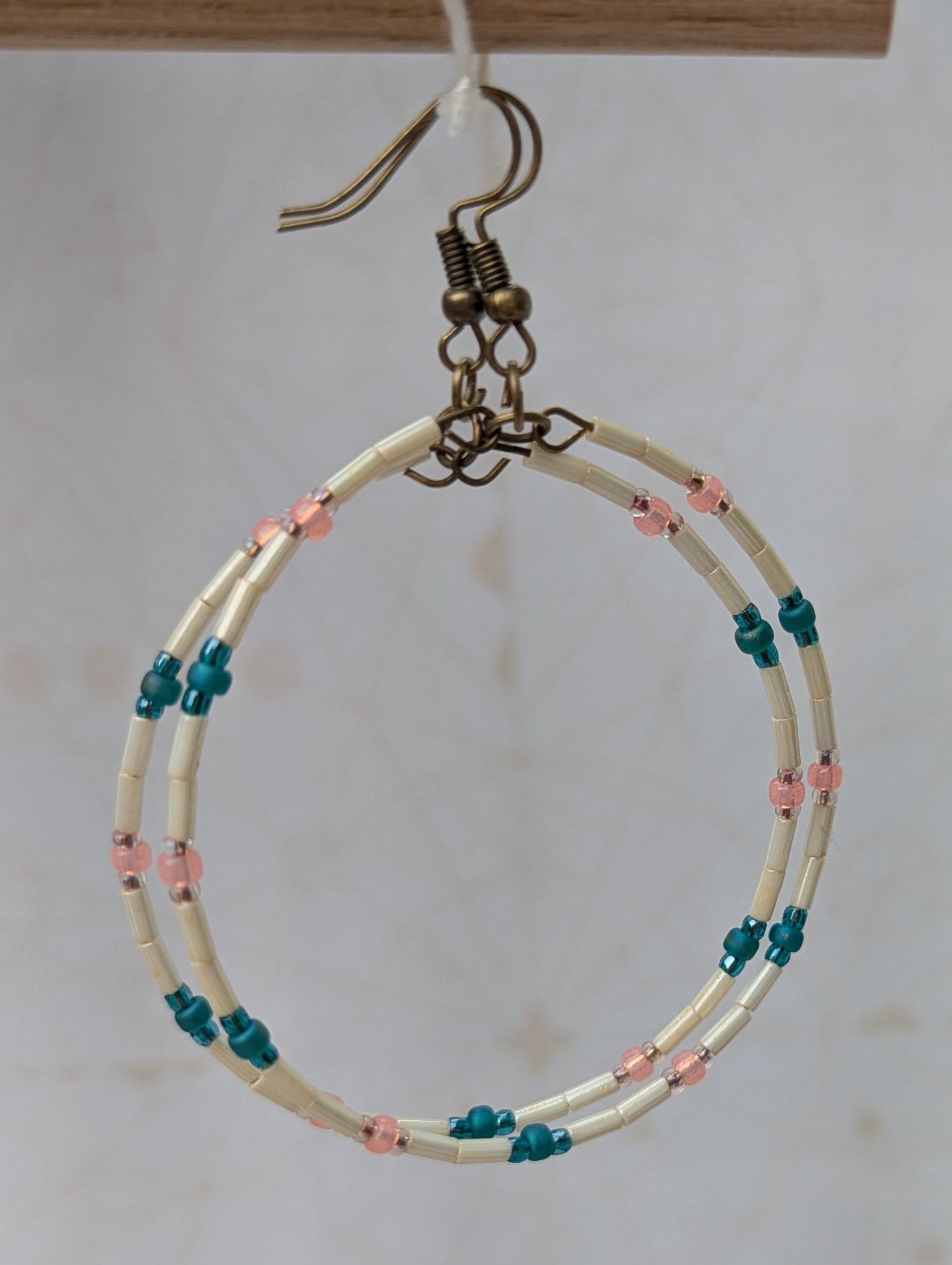 Handmade ivory hoop earrings with blush pink and teal glass bead accents on bronze memory wire and bronze French hooks.