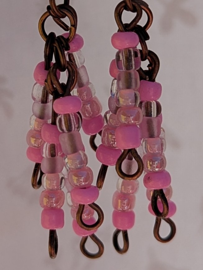 Handmade bronze-tone fringe earrings with soft pink and iridescent blush glass beads hanging in cascading strands from bronze-colored French hooks.