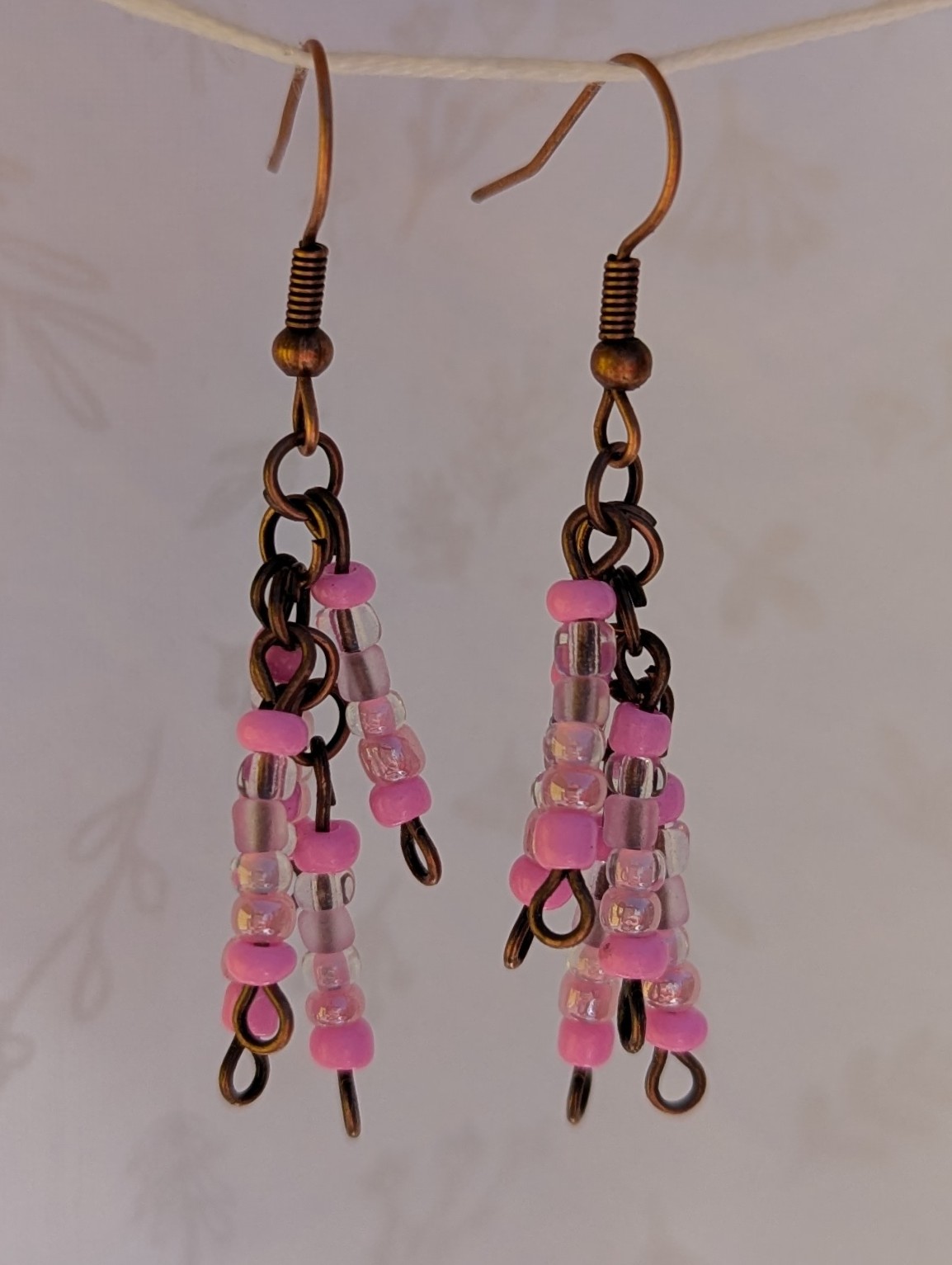 Handmade bronze-tone fringe earrings with soft pink and iridescent blush glass beads hanging in cascading strands from bronze-colored French hooks.