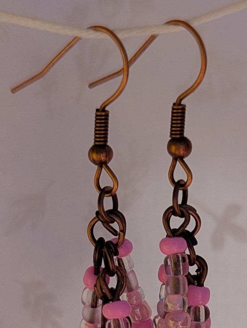 Handmade bronze-tone fringe earrings with soft pink and iridescent blush glass beads hanging in cascading strands from bronze-colored French hooks.