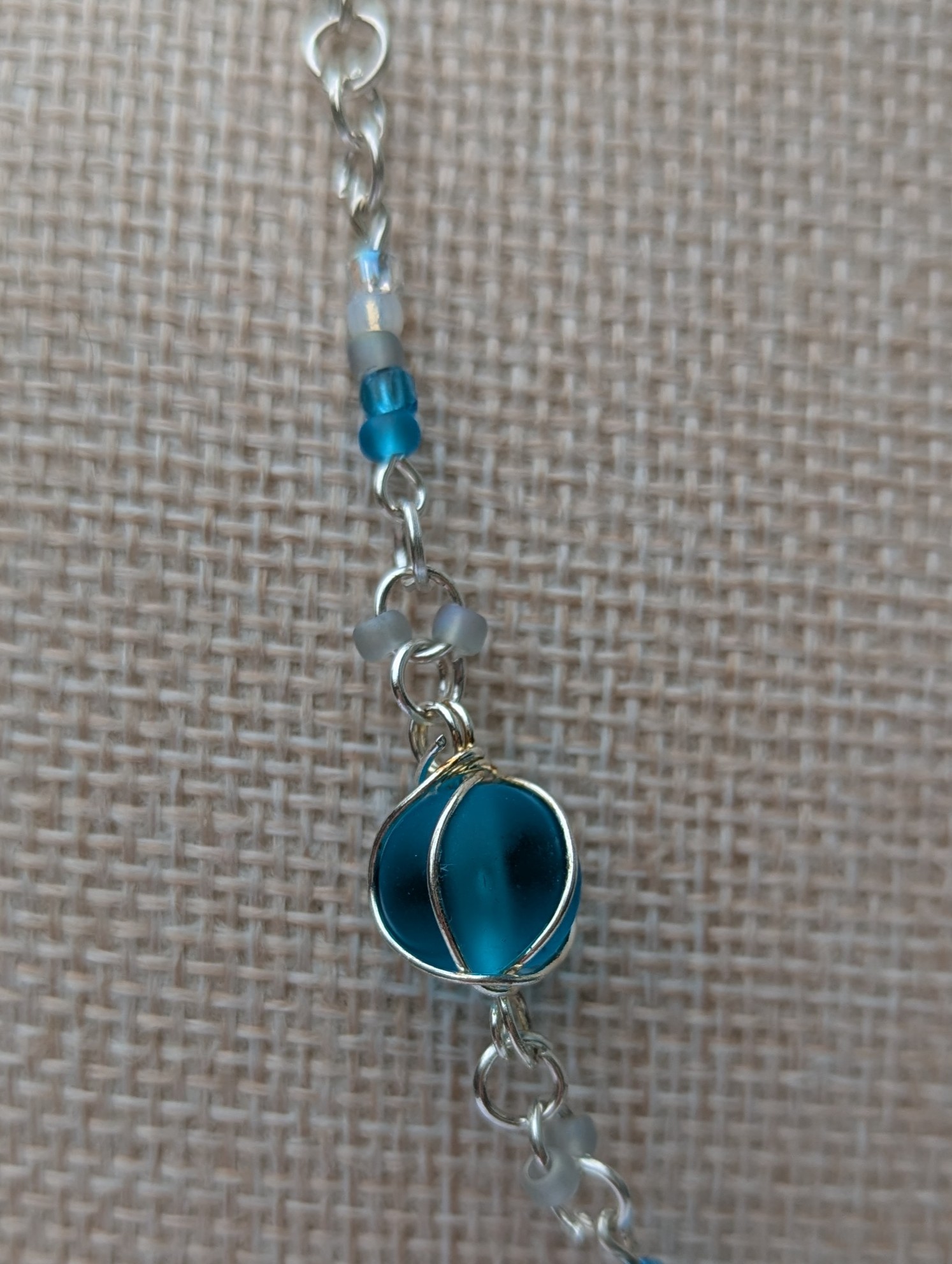 Handmade silver-colored chain necklace with pale aqua and frosted white seed beads, featuring three wire-wrapped ocean-blue glass beads and a silver lobster clasp closure.