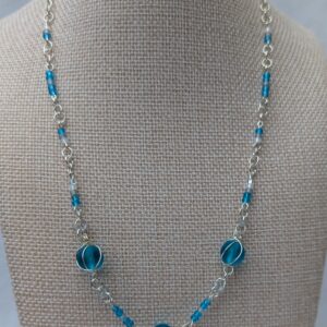 Handmade silver-colored chain necklace with pale aqua and frosted white seed beads, featuring three wire-wrapped ocean-blue glass beads and a silver lobster clasp closure.
