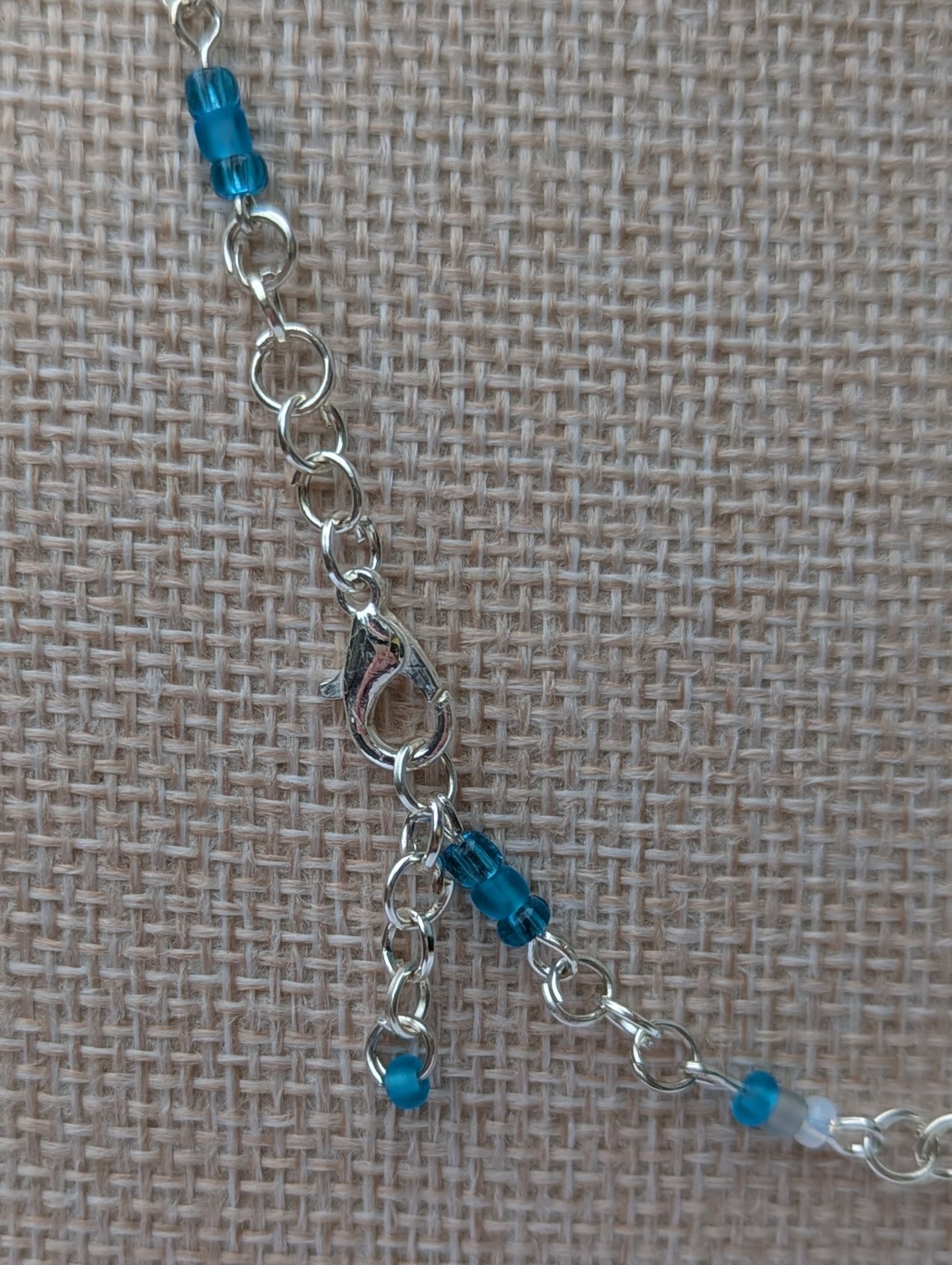 Handmade silver-colored chain necklace with pale aqua and frosted white seed beads, featuring three wire-wrapped ocean-blue glass beads and a silver lobster clasp closure.