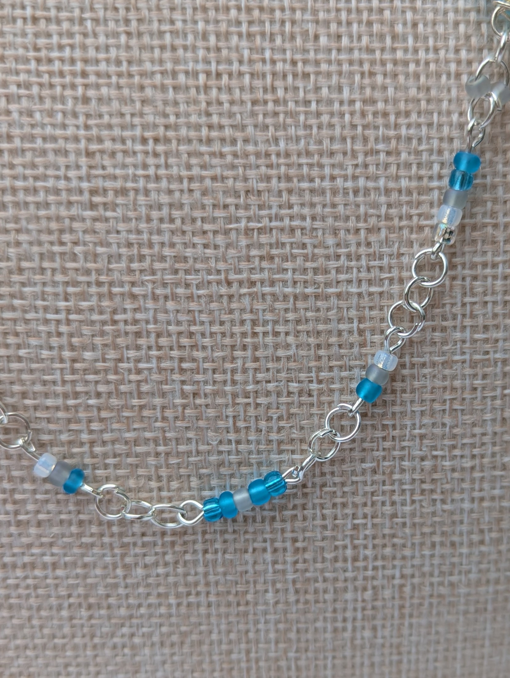 Handmade silver-colored chain necklace with pale aqua and frosted white seed beads, featuring three wire-wrapped ocean-blue glass beads and a silver lobster clasp closure.