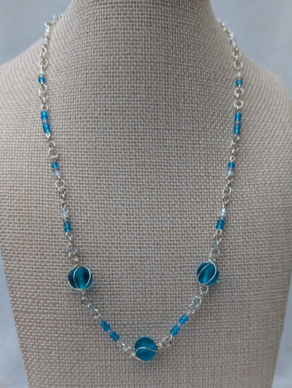 Handmade silver-colored chain necklace with pale aqua and frosted white seed beads, featuring three wire-wrapped ocean-blue glass beads and a silver lobster clasp closure.