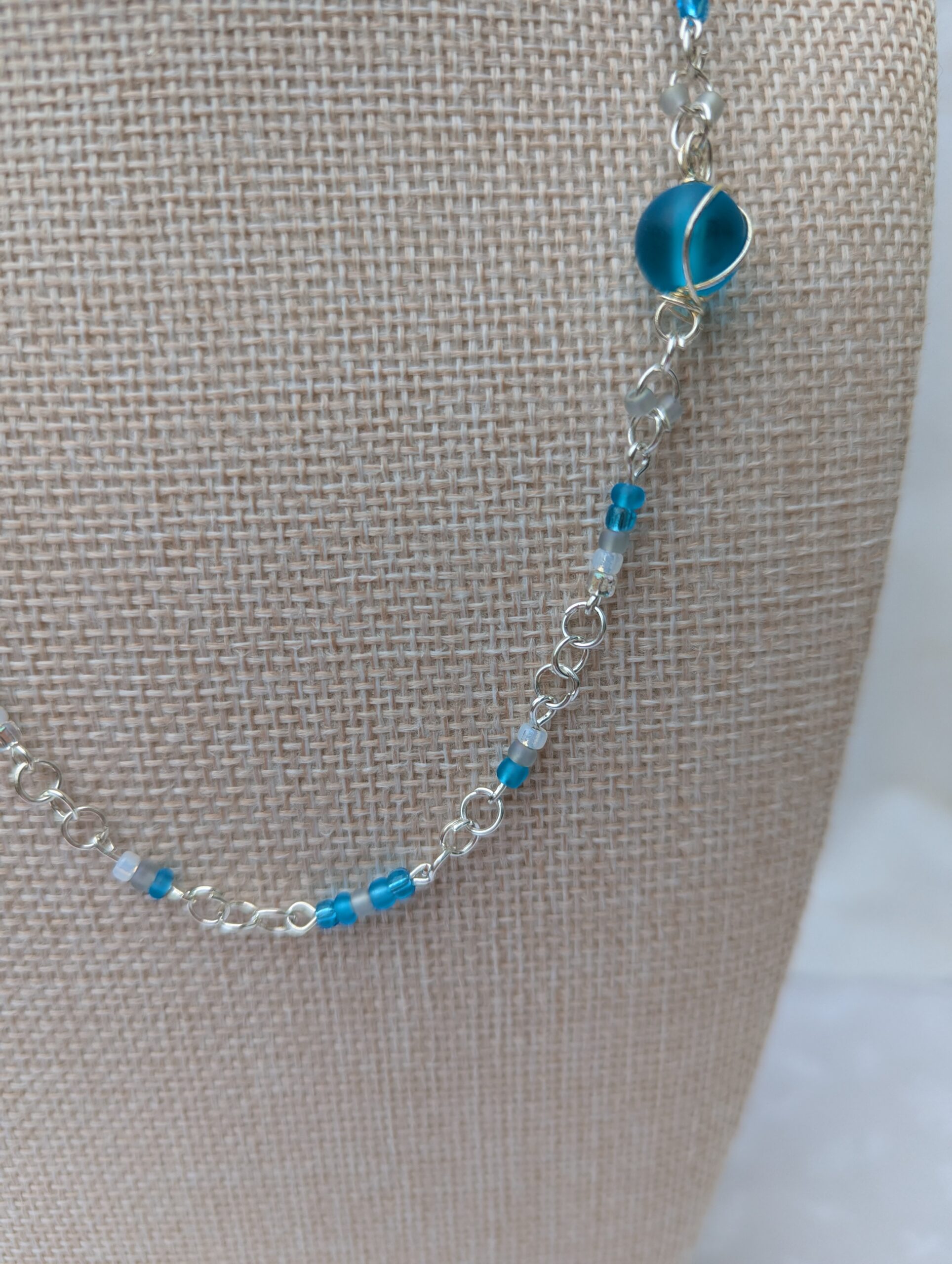 Handmade silver-colored chain necklace with pale aqua and frosted white seed beads, featuring three wire-wrapped ocean-blue glass beads and a silver lobster clasp closure.